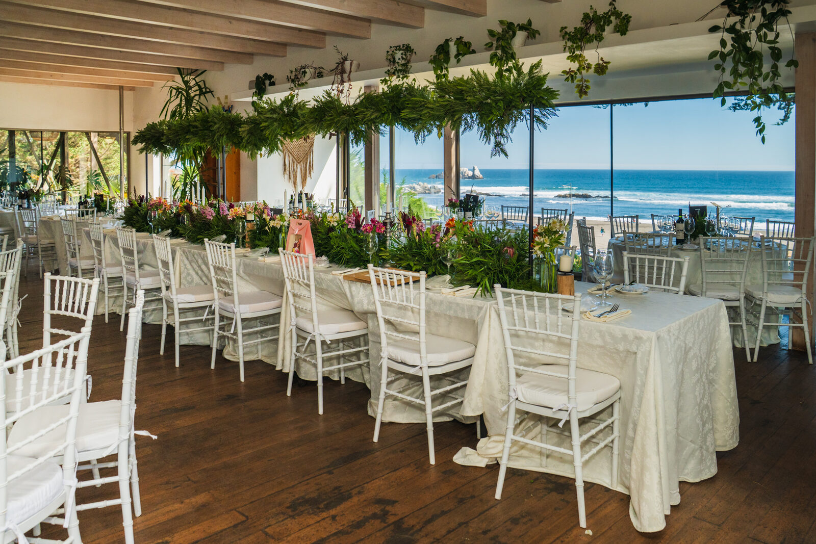 Mesa larga de banquete con guirnalda floral y vista al mar